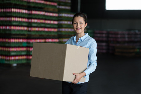 Portrait of female factory worker carrying cardboard boxes in factoryの写真素材