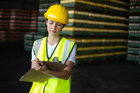 Attentive female factory worker writing on clipboard in factoryの写真素材