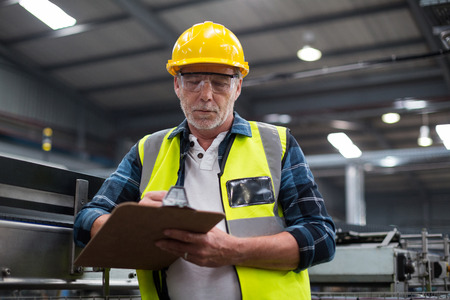 Male factory worker maintaining record on clipboard in drinks production factoryの写真素材