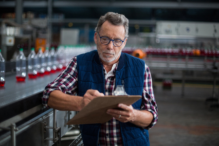 Male factory worker maintaining record on clipboard in drinks production factoryの写真素材