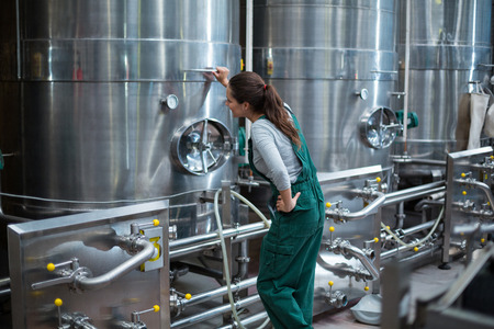 Female factory worker looking at control wheel of storage tank at drinks production factoryの写真素材