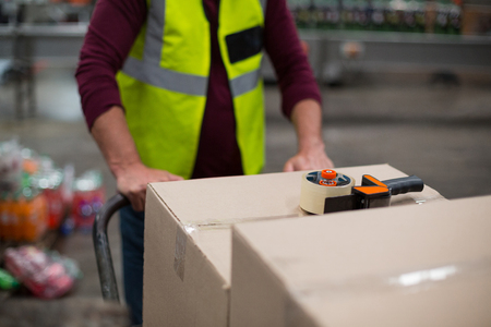 Mid section of factory worker pulling trolley of cardboard boxes in drinks production factoryの写真素材