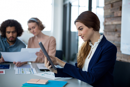 Female business executive using digital tablet in office and colleague discussing in backgroundの写真素材