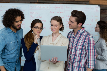 Business team discussing over laptop while colleague working in background at office