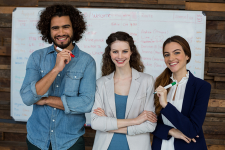 Portrait of smiling business executives standing against white board in officeの写真素材