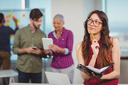 Thoughtful female business executive holding organizer in officeの写真素材