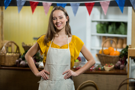 Portrait of smiling woman vendor standing in the grocery store with hands on hips
