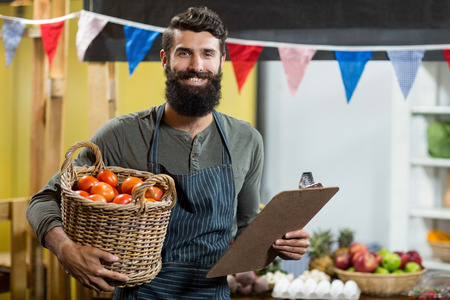 Portrait of a vendor holding a clipboard and a basket of tomatoes at the grocery storeの写真素材