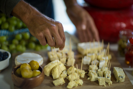 Close-up of staff arranging piece of cheese on wooden board in grocery shopの写真素材