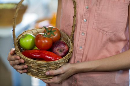 Mid-section of woman holding a basket with variety of fruits and vegetablesの写真素材