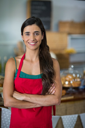 Portrait of female staff standing with arms crossed at counter in bake shopの写真素材