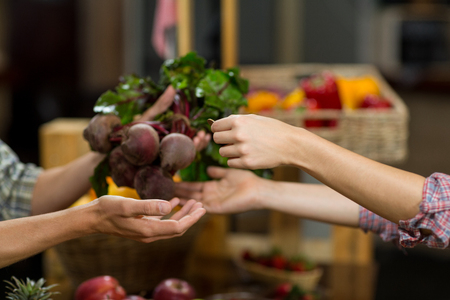 Close-up of a woman buying beetroot from vendor in the grocery storeの写真素材