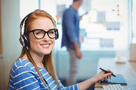 Female graphic designer working with headphones in officeの写真素材