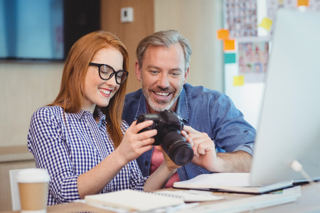 Two graphic designers looking at pictures in digital camera at officeの写真素材