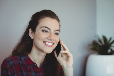 Smiling female executive talking on mobile phone in officeの写真素材