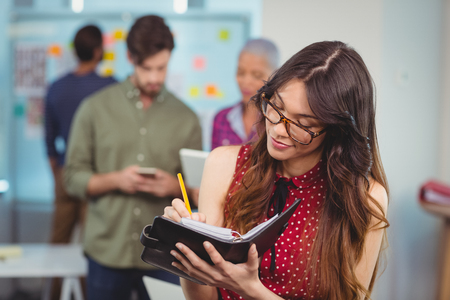 Female executive writing in organizer in officeの写真素材
