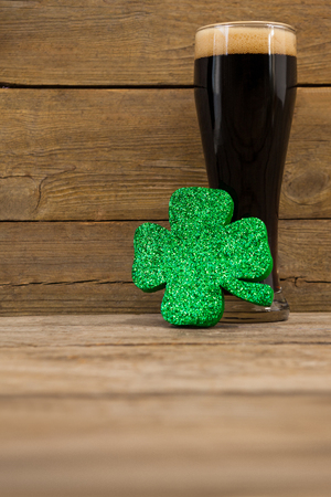 Glass of black beer and shamrock for St Patricks Day against wooden backgroundの写真素材
