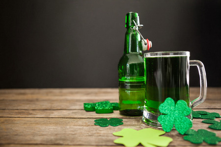 Mug of green beer, beer bottle and shamrocks for St Patricks Day on wooden tableの写真素材