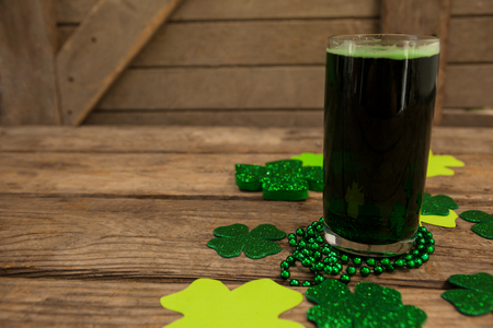 Glass of green beer, beads and shamrock for St Patricks Day on wooden tableの写真素材