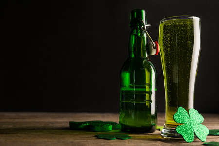 Glass of green beer, beer bottle and shamrocks for St Patricks Day on wooden tableの写真素材