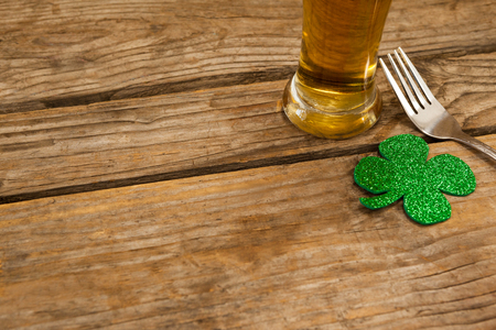 Glass of beer, fork and shamrock for St Patricks Day against wooden backgroundの写真素材
