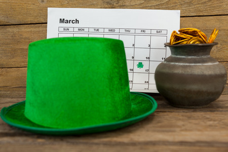 St. Patricks Day leprechaun hat with calendar and pot filled with chocolate gold coins on wooden tableの写真素材