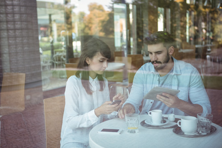 Attentive executives using mobile phone and digital tablet in cafÃ©
