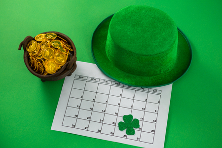 St. Patricks Day leprechaun hat with shamrock, calendar and pot with chocolate gold coins on green backgroundの写真素材