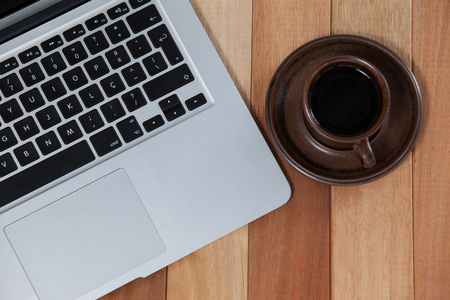 Cup of black coffee and laptop on wooden backgroundの写真素材
