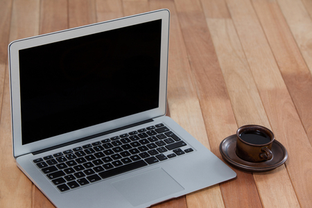 Cup of black coffee and laptop on wooden backgroundの写真素材