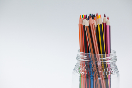 Colored pencils kept in a glass jar on white backgroundの写真素材