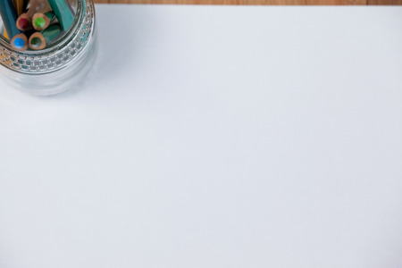 Jar of colored pencils kept on white paper on wooden background