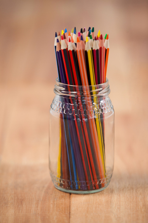 Colored pencils kept in a glass jar on wooden backgroundの写真素材