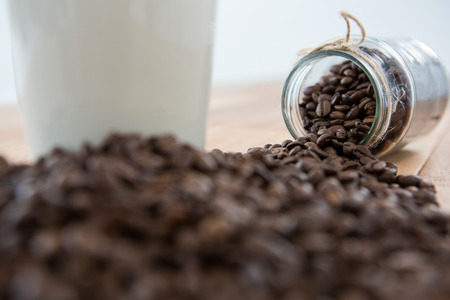 Close-up of coffee beans spilling out of jar on wooden tableの写真素材