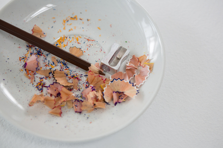 Colored shavings with brown color pencil and sharpener in saucer on white backgroundの写真素材