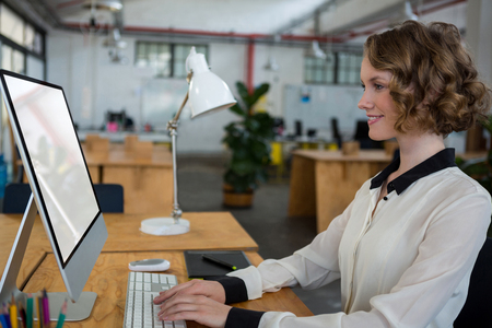Female graphic designer using desktop pc in creative officeの写真素材