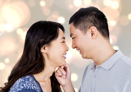 Digital composite of  happy asian couple looking each other against bright backgroundの写真素材