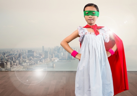 Portrait of super kid in red cape and green mask standing with hand on hip against digitally composite cityscapeの写真素材