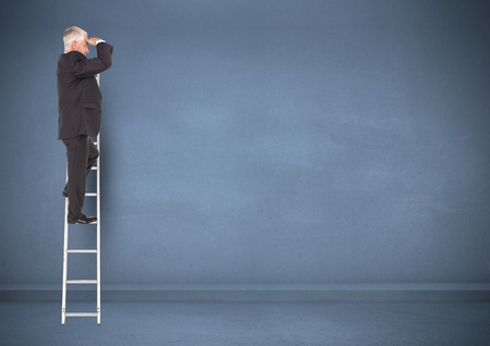Businessman on ladder looking at a distance against blue backgroundの写真素材