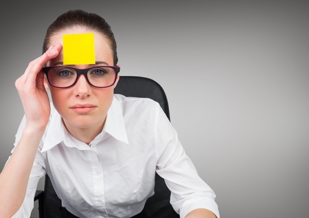 Serious businesswoman with sticky note on her forehead against grey backgroundの写真素材
