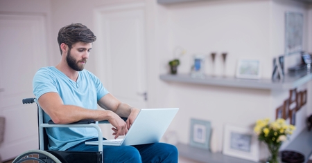 Digital composition of man sitting on wheelchair and using laptop at homeの写真素材
