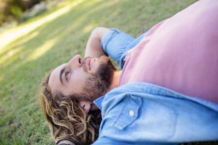 Thoughtful man lying on grass with hand behind head in parkの写真素材