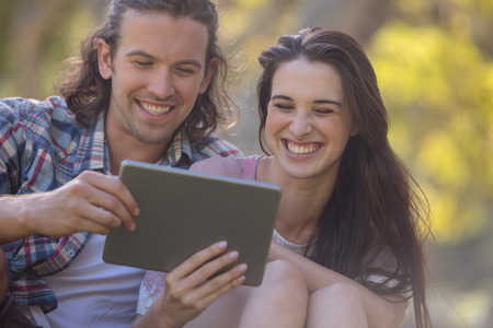 Couple sitting on grass and using digital tablet in park on a sunny day