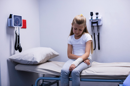 Girl with injured hand sitting on stretcher bed in hospitalの写真素材