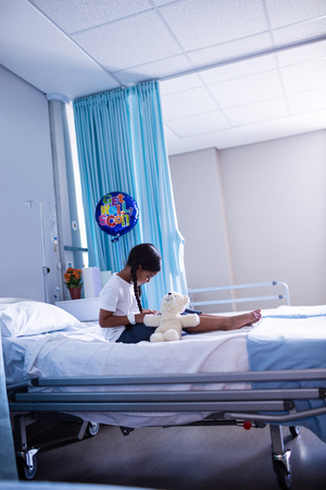 Patient sitting on bed with teddy bear in hospitalの写真素材