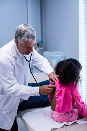 Doctor examining patient with stethoscope at hospitalの写真素材
