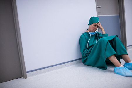 Tensed female surgeon sitting in corridor of hospitalの写真素材