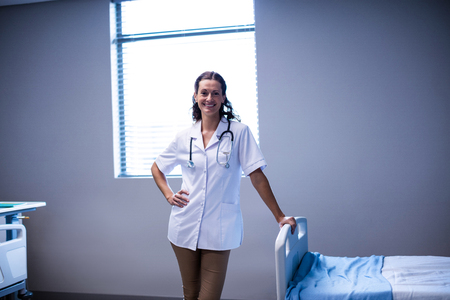 Portrait of female doctor standing with hand on hip in ward of hospitalの写真素材