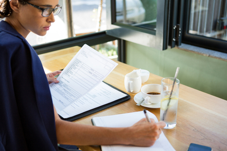 Focused female executive writing in diary at caféの写真素材