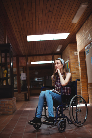 Thoughtful disabled schoolboy on wheelchair in corridor at schoolの写真素材